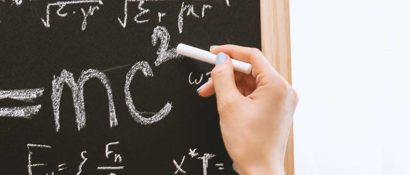 A hand writing mathematical equations on a chalk board.